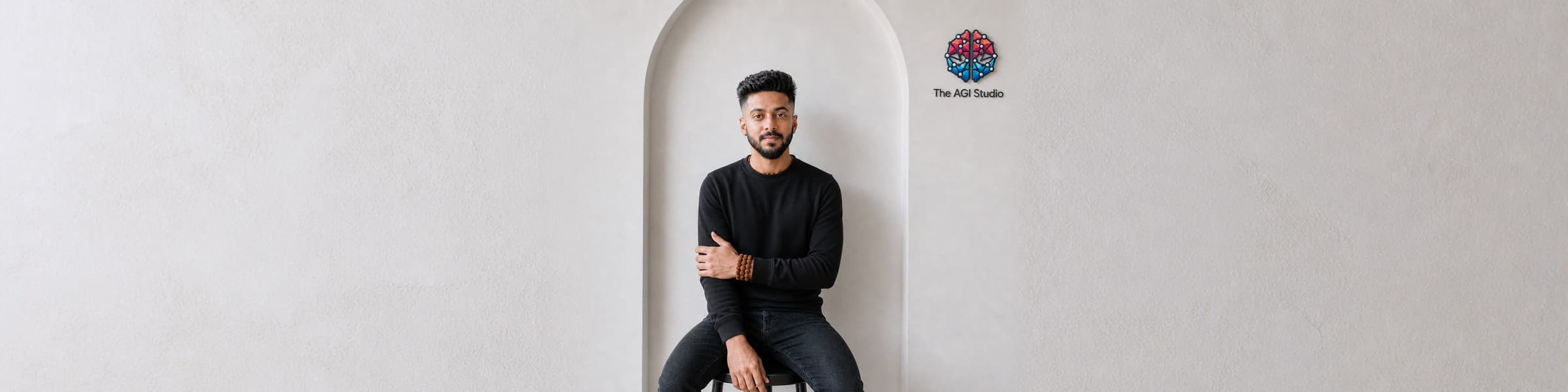 Shrish Manglik seated in the studio's arch, the AGI Studio mark on the wall beside him